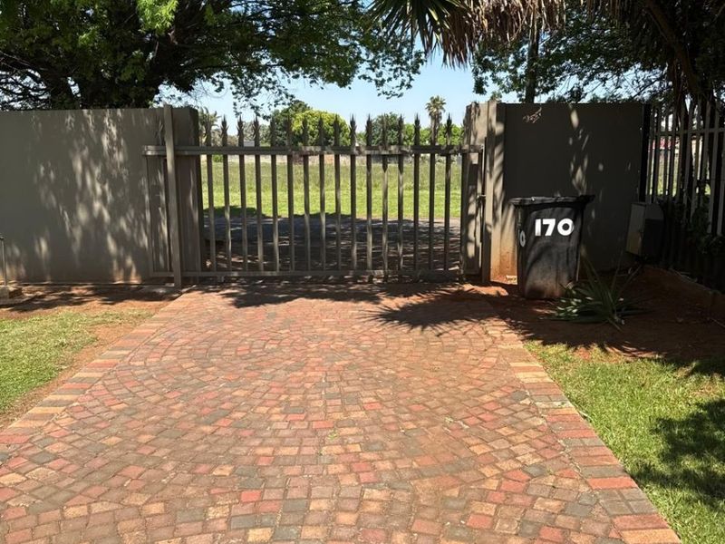 A paved driveway leading to a secure metal gate and boundary wall, surrounded by established trees and lawn.