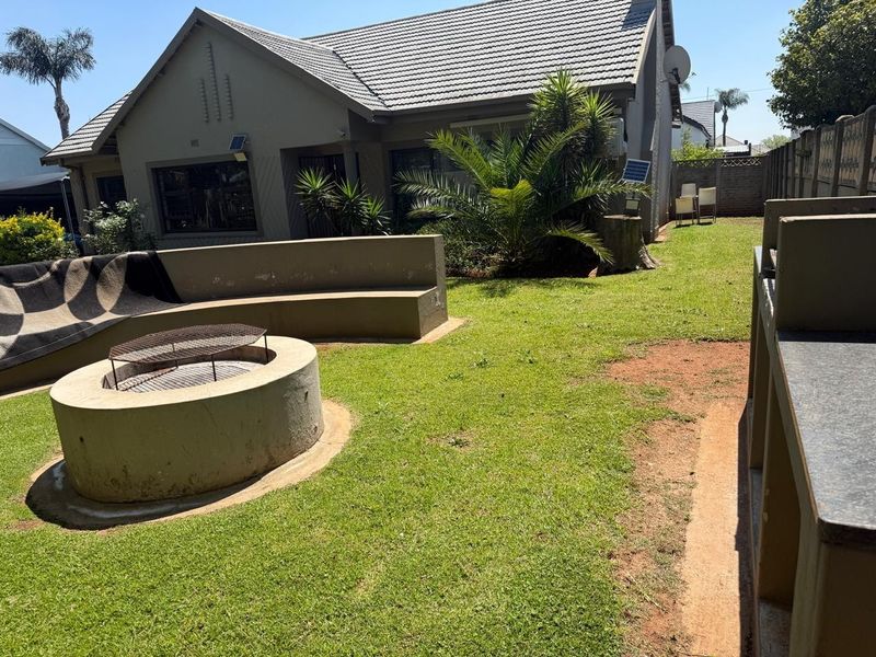 Rear garden featuring a built-in fire pit with curved bench seating and a dedicated outdoor braai area, set against the rear facade of the house.