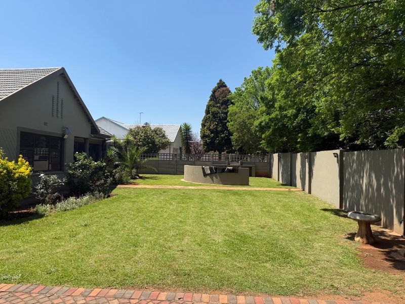 A well-maintained rear garden featuring a lawn, paved walkway, perimeter wall, and a built-in braai area, perfect for outdoor entertaining.