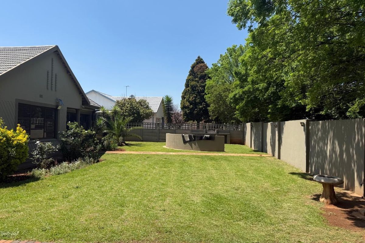 A well-maintained rear garden featuring a lawn, paved walkway, perimeter wall, and a built-in braai area, perfect for outdoor entertaining.