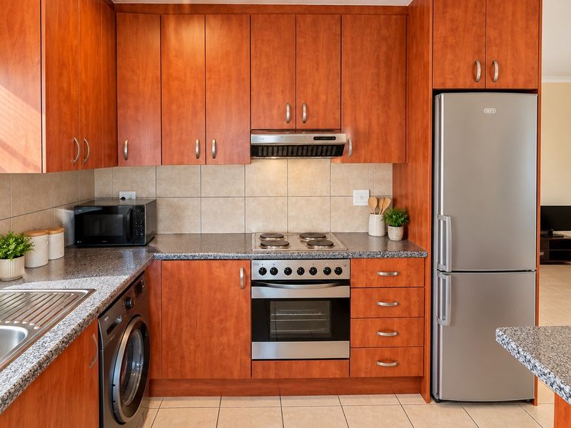A well-maintained kitchen featuring warm-toned wooden cabinetry, granite countertops, a stainless steel oven with hob, and integrated laundry plumbing.