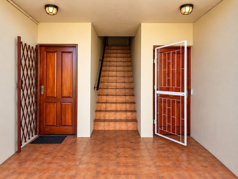 A clean and well-maintained entrance area featuring tiled flooring, secure timber doors with security gates, and a central staircase leading to the upper level.