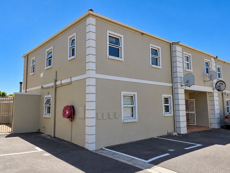 Exterior view of a two-story apartment building featuring a paved parking area, designated bays, and secure gated access.
