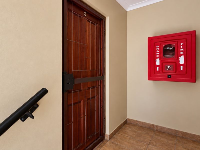 Apartment entrance featuring a secure wooden door with a security gate, tiled flooring, and a wall-mounted fire safety cabinet.