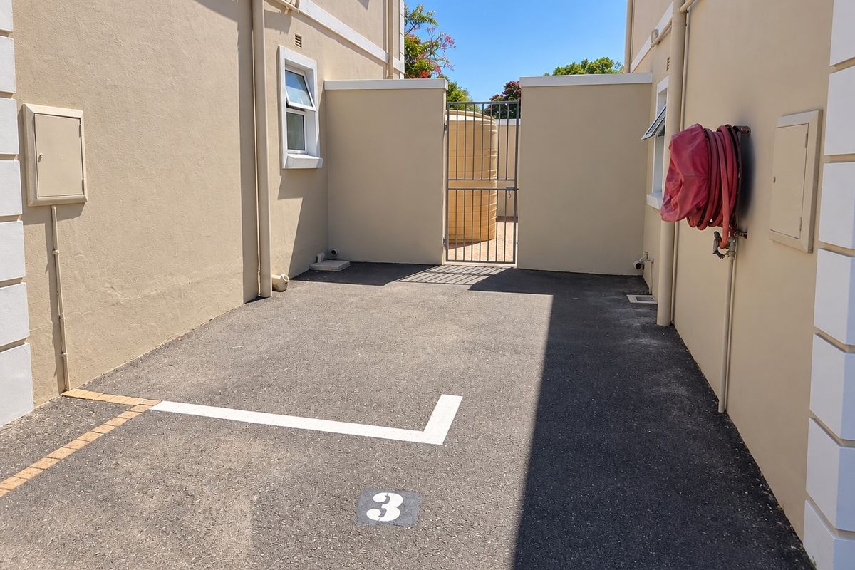 A clean and well-maintained rear exterior area featuring a designated parking space, boundary walls, and a secure gated access point to a water tank.