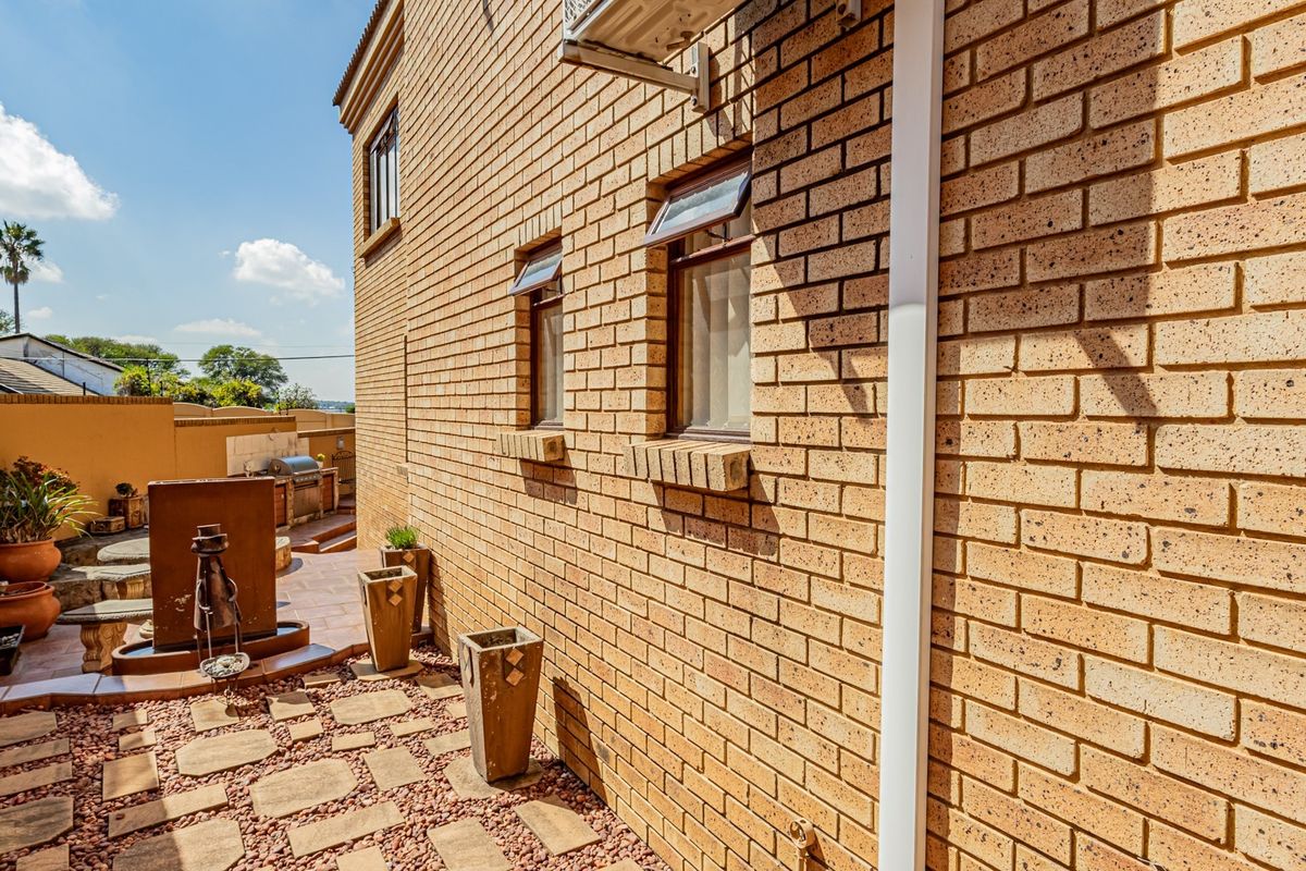 A side view of the property featuring face brick walls, top-hung windows, and a paved rear patio area with a built-in braai.