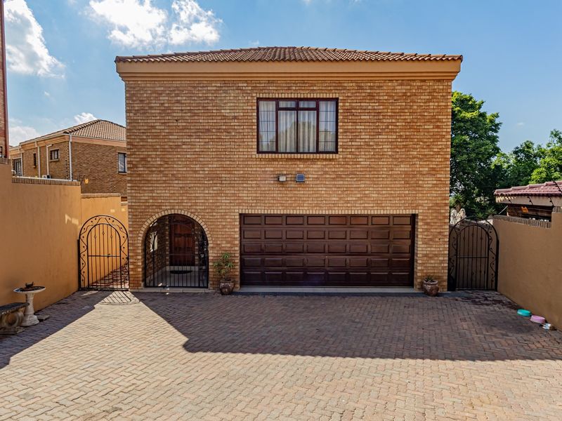 Front elevation of a double-storey brick house featuring a paved driveway, double garage, and arched entrance with secure perimeter walling.