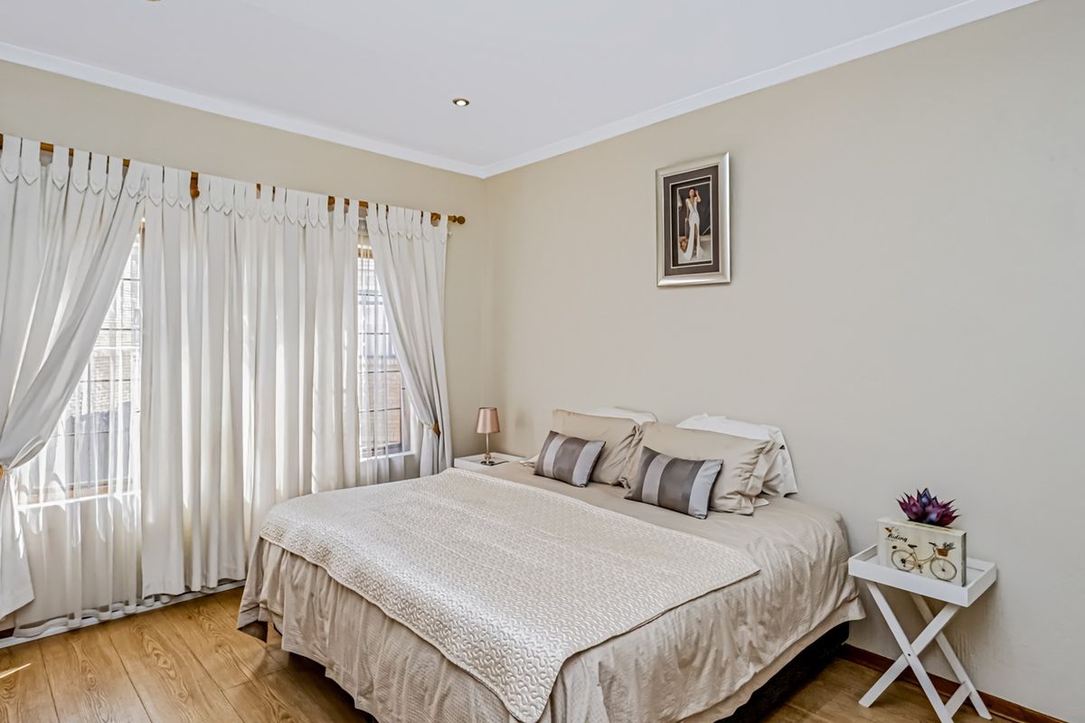 A well-maintained bedroom featuring neutral wall tones, laminate flooring, and large windows with curtain treatments.