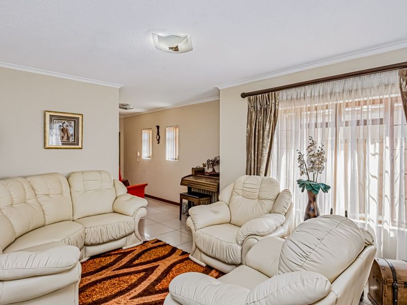 A comfortable living room featuring tiled flooring, neutral wall tones, and large windows dressed with curtains and blinds, offering a bright and inviting space.