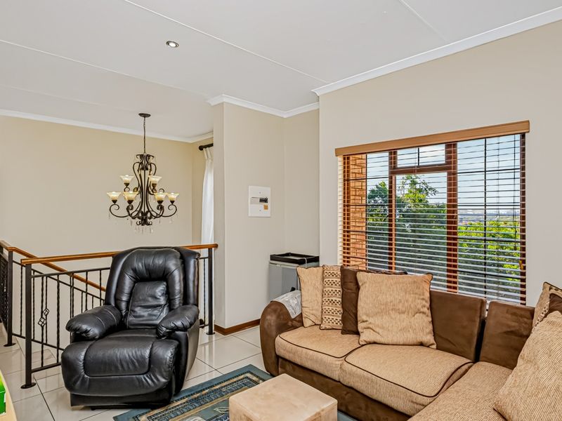 A bright living area featuring tiled flooring, recessed lighting, and a staircase with a decorative wrought iron railing overlooking the space.