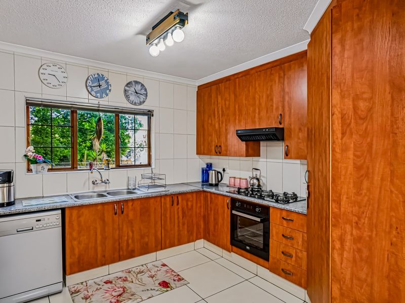 Functional kitchen featuring warm-toned wooden cabinetry, laminate countertops, a gas hob with extractor fan, and a double basin sink with garden views.