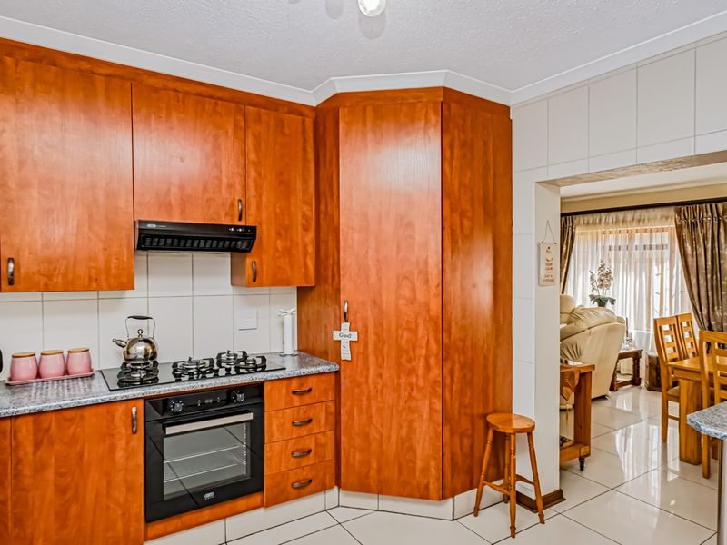 A functional kitchen featuring warm-toned wooden cabinetry, a built-in oven with gas hob, and tiled flooring, seamlessly connecting to the adjacent dining area.