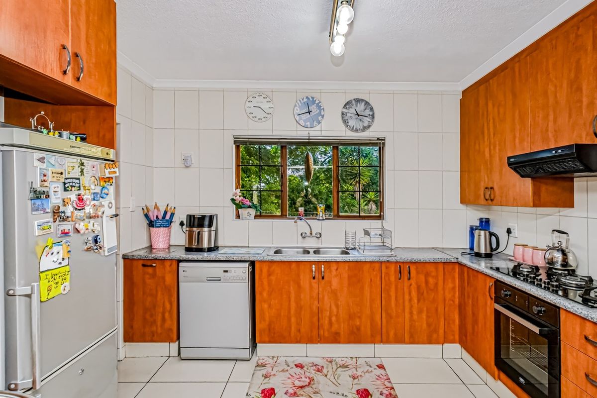 A functional kitchen featuring wooden cabinetry, tiled backsplash, built-in oven with gas hob, and a double sink overlooking the garden.