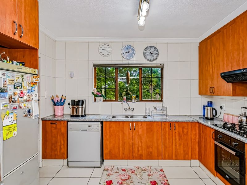 A functional kitchen featuring wooden cabinetry, tiled backsplash, built-in oven with gas hob, and a double sink overlooking the garden.