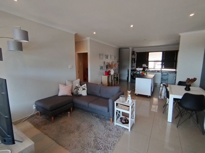 An open-plan living and kitchen area featuring tiled flooring, recessed lighting, and a functional kitchen island, creating a cohesive and modern living space.