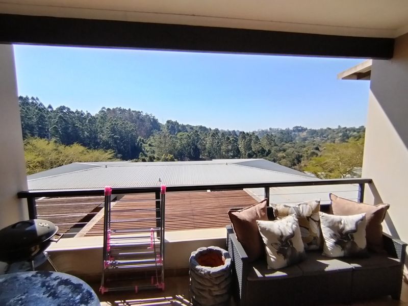 A covered balcony featuring a metal railing and expansive views of the surrounding forest and landscape.
