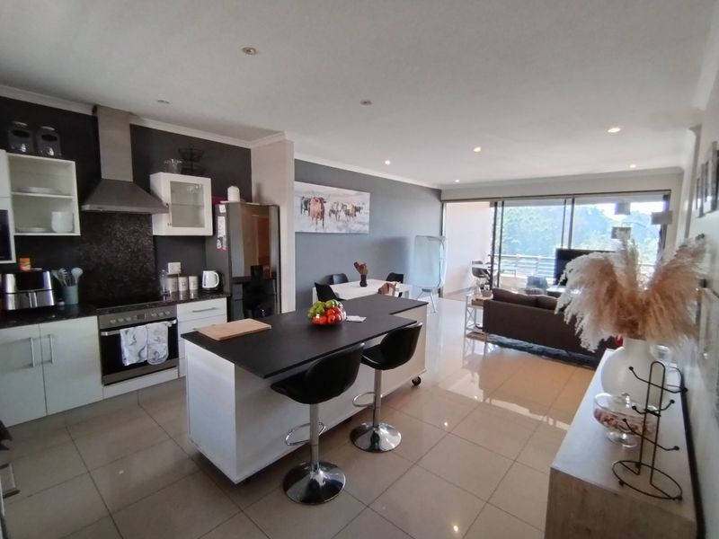 Spacious open-plan living area featuring a modern kitchen with a central island, sleek cabinetry, and seamless flow to the outdoor balcony.
