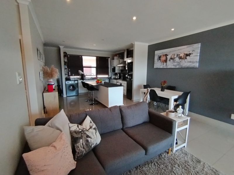 Open-plan living area featuring a modern kitchen with a central island, integrated cabinetry, and tiled flooring, seamlessly connecting to the dining and lounge space.
