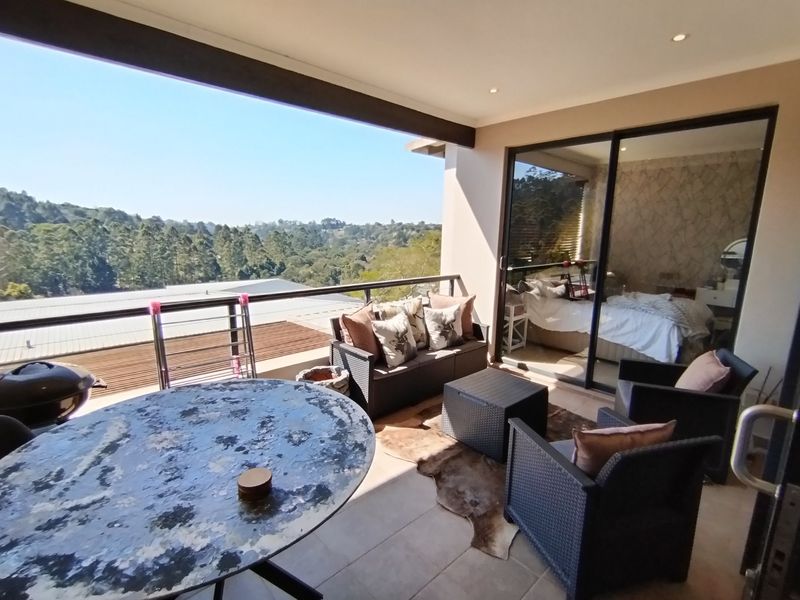 A spacious covered balcony featuring tiled flooring, recessed lighting, and a metal balustrade, offering scenic views and direct access to the interior living space.