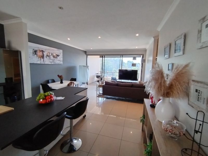 Spacious open-plan living area featuring a modern kitchen island, sleek tiled flooring, and large sliding glass doors leading to an outdoor balcony.