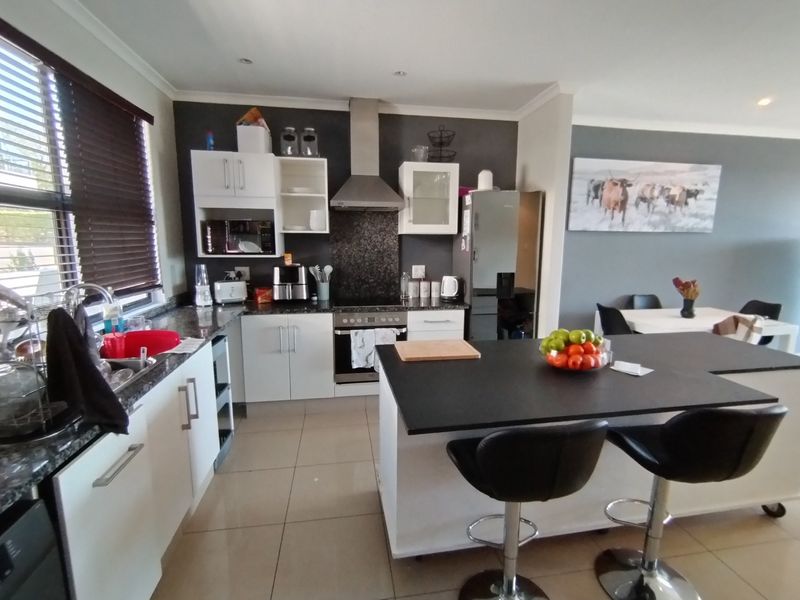 Modern open-plan kitchen featuring a central island, granite countertops, built-in oven, and sleek white cabinetry, seamlessly flowing into the dining area.