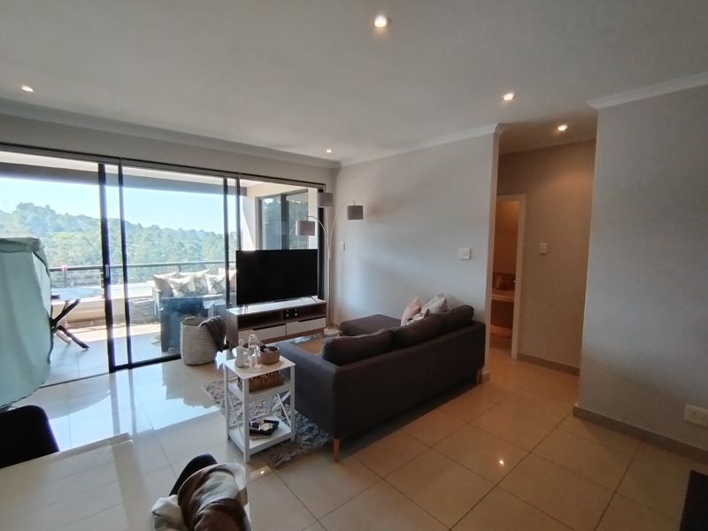 A bright, open-plan living area featuring tiled floors, recessed lighting, and large sliding glass doors that provide access to an outdoor balcony.