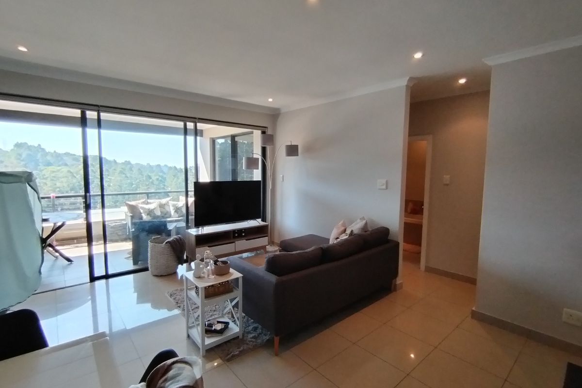 A bright, open-plan living area featuring tiled floors, recessed lighting, and large sliding glass doors that provide access to an outdoor balcony.
