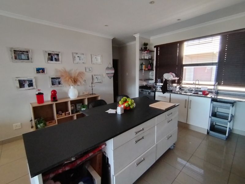 A functional kitchen featuring a central island with a dark countertop, white cabinetry, tiled flooring, and large windows with venetian blinds.