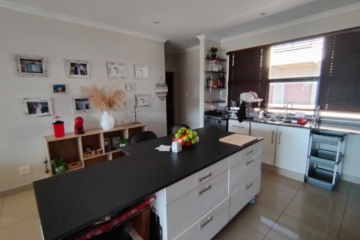 A functional kitchen featuring a central island with a dark countertop, white cabinetry, tiled flooring, and large windows with venetian blinds.