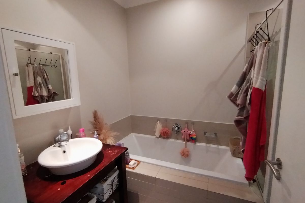 A functional bathroom featuring a built-in bathtub with tiled surround, a vanity basin, and a wall-mounted mirror cabinet.