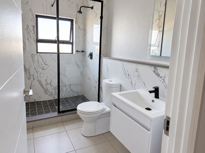 Modern bathroom featuring a walk-in shower with black-framed glass, marble-look wall tiling, a sleek vanity unit, and contemporary black fixtures.