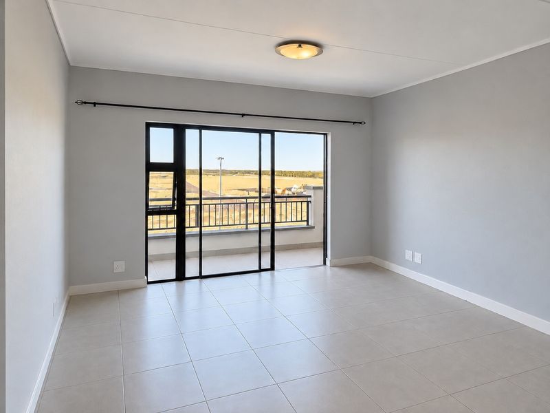 A bright, empty living room featuring neutral tiled flooring, modern grey walls, and a large sliding glass door leading to a balcony.