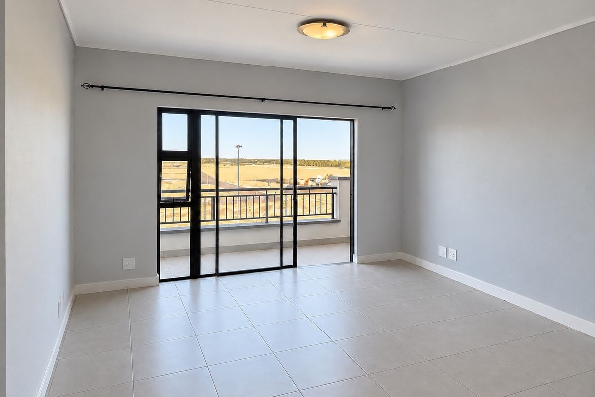A bright, empty living room featuring neutral tiled flooring, modern grey walls, and a large sliding glass door leading to a balcony.