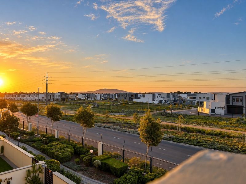 A scenic sunset view overlooking a suburban street, landscaped green belts, and surrounding residential estate architecture.