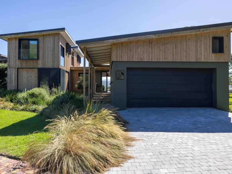 Modern architectural house exterior featuring timber cladding, a paved driveway, and a spacious garage, set within a well-maintained landscaped garden.