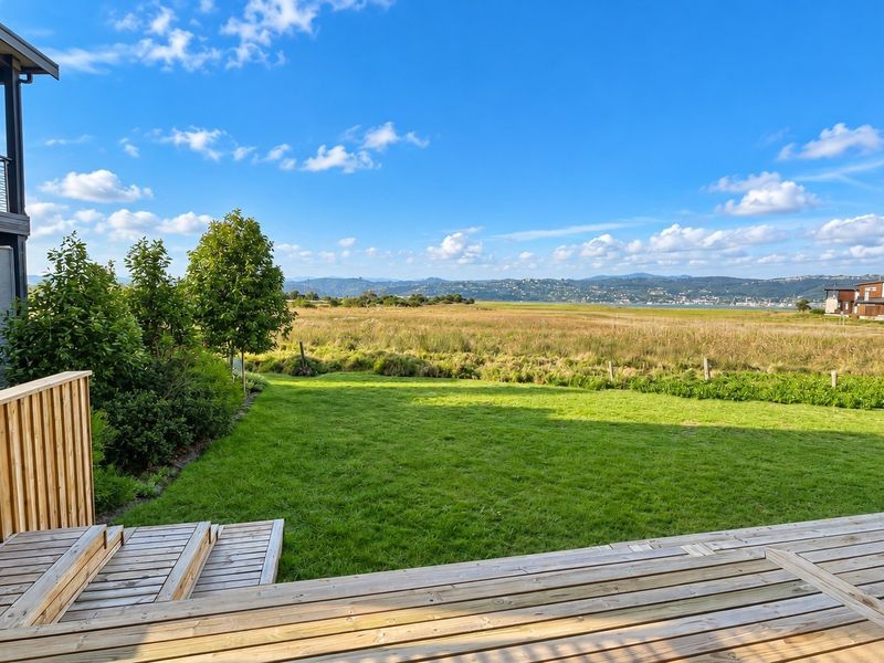 A well-maintained timber deck featuring a balustrade and stairs, overlooking a lush green lawn and expansive natural landscape views.