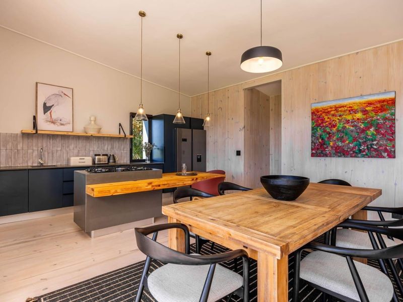 Modern open-plan kitchen and dining area featuring sleek dark cabinetry, a gas hob, timber wall accents, and contemporary pendant lighting.