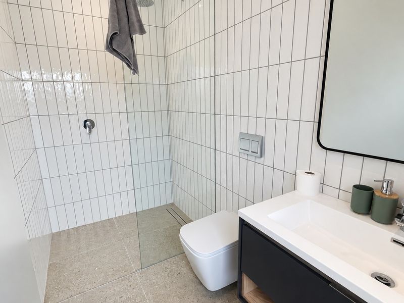 Modern bathroom featuring a walk-in shower with glass screen, wall-mounted toilet, and a sleek vanity unit with integrated basin.