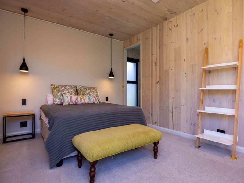 A modern bedroom featuring a warm timber-clad ceiling and feature wall, complemented by contemporary pendant lighting and neutral carpeting.