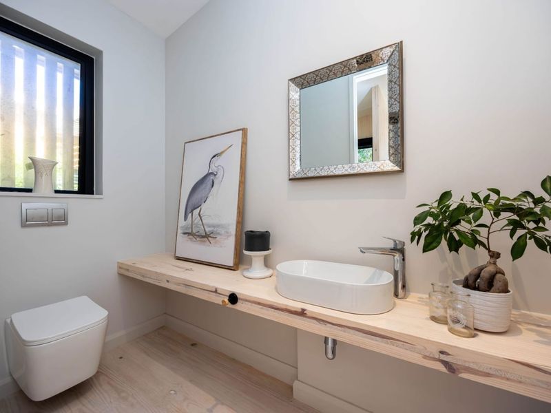 Modern guest bathroom featuring a wall-hung toilet, timber vanity shelf with a sleek countertop basin, and contemporary chrome fixtures.