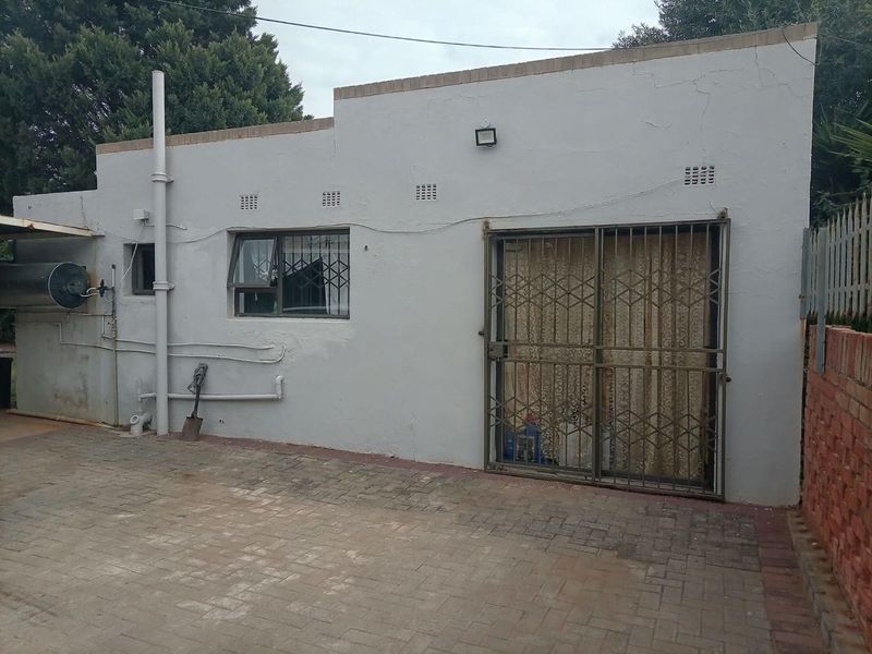 Rear exterior view of the property featuring a paved area, sliding door with security gate, and external plumbing fixtures.