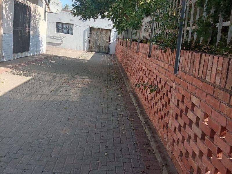 A paved side driveway featuring a decorative brick boundary wall, security gate, and access to the rear of the property.