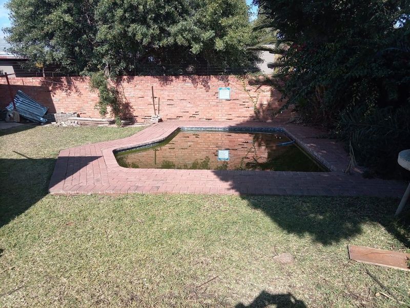 Outdoor swimming pool area featuring brick paving and a perimeter brick boundary wall, currently requiring maintenance and pool water treatment.