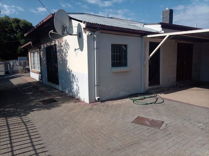Rear exterior view of the property featuring a paved courtyard, corrugated metal roof, and security-fitted windows.