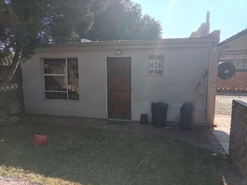 Rear view of a detached outbuilding featuring a corrugated metal roof, security-fitted windows, and a wooden entrance door set against a small garden area.