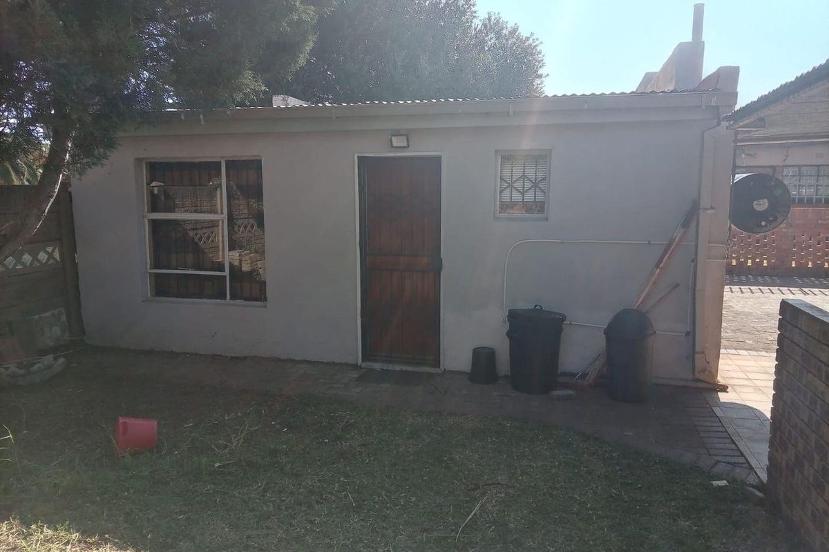 Rear view of a detached outbuilding featuring a corrugated metal roof, security-fitted windows, and a wooden entrance door set against a small garden area.
