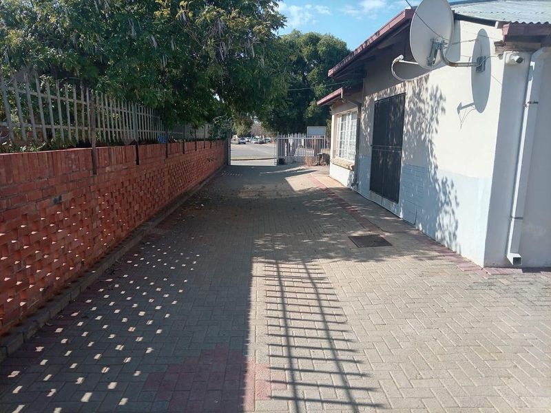 A paved driveway leading to a secure metal gate, featuring a brick boundary wall and exterior building access with security fixtures.