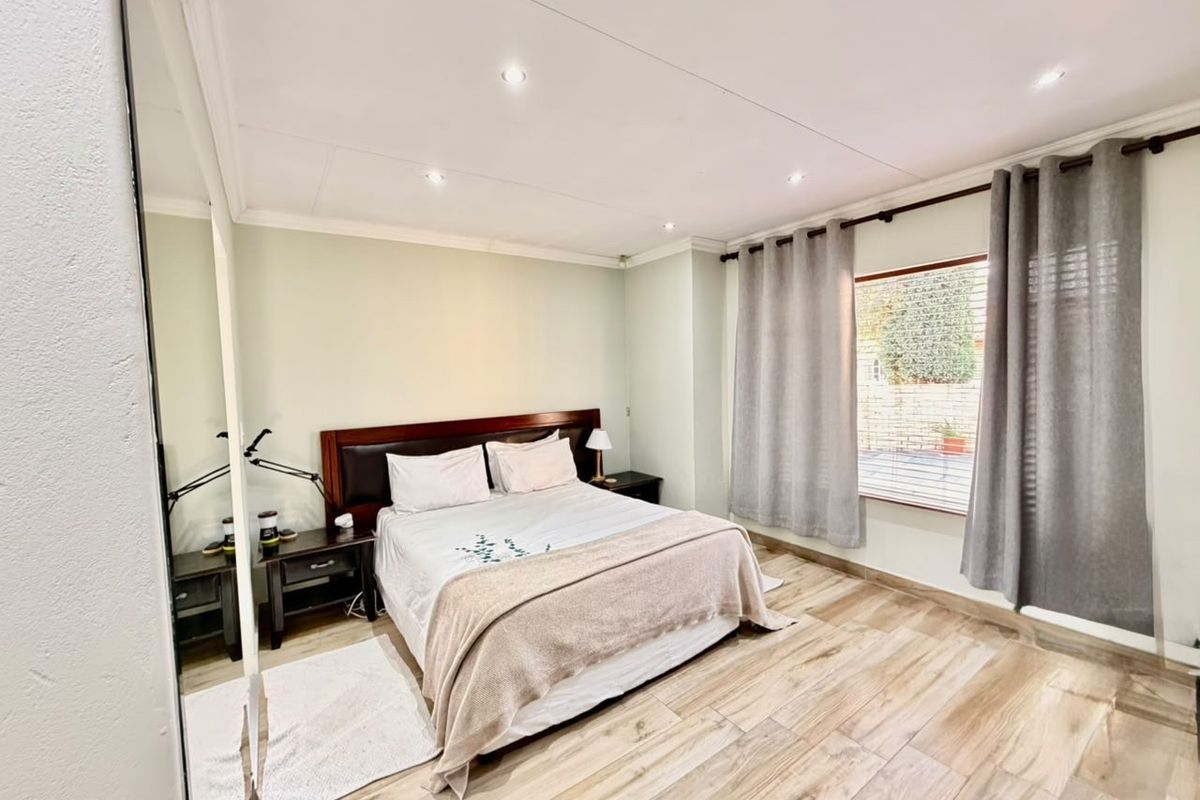 A well-maintained bedroom featuring wood-look tile flooring, recessed downlighting, and a built-in cupboard with mirrored doors, offering a bright and functional living space.