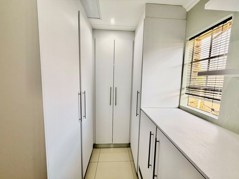 A clean, functional utility space or dressing area featuring extensive built-in white cabinetry, tiled flooring, and natural light from a side window.