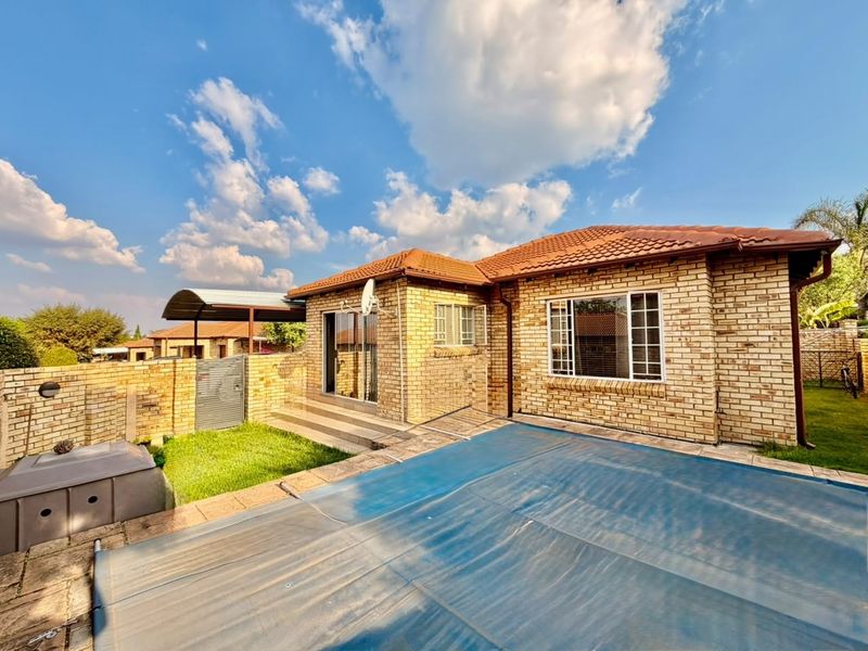 Rear view of a face brick house featuring a swimming pool with cover, paved patio area, and an attached carport.